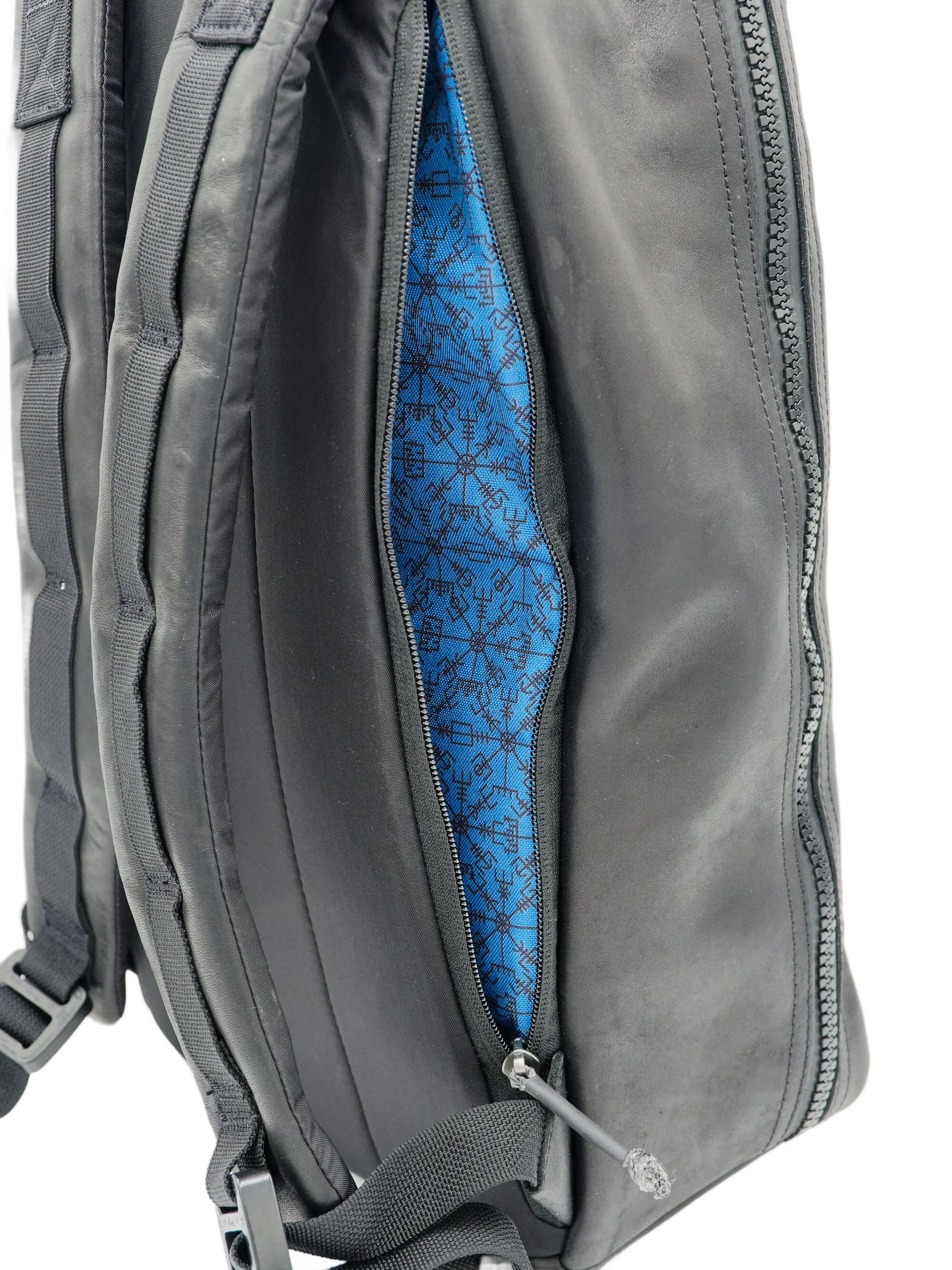 Close-up of the side zipper partially open revealing the blue patterned interior lining of the leather backpack