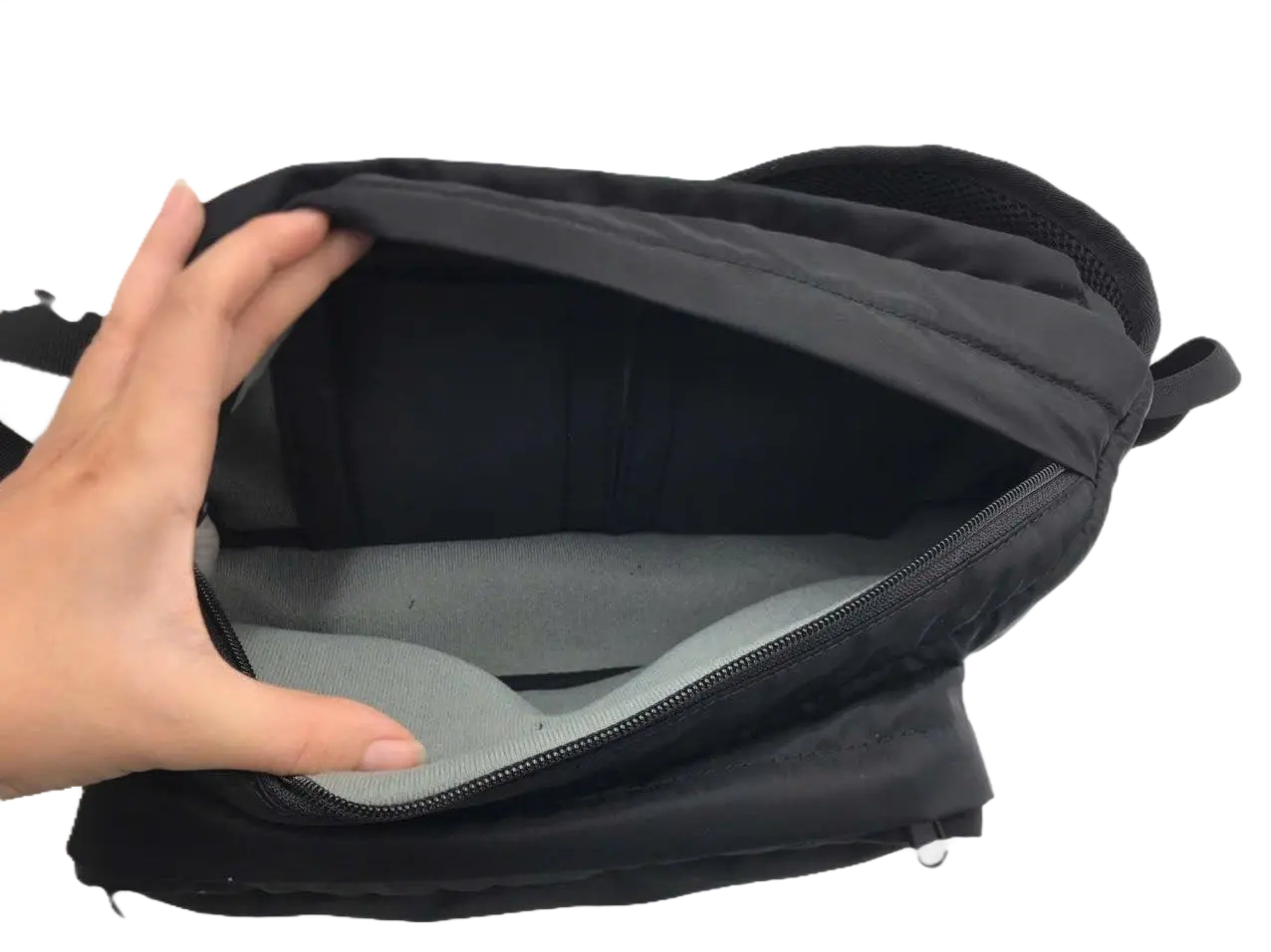 Hand opening the main compartment of the black sling pack revealing a grey padded lining with a zipped internal divider