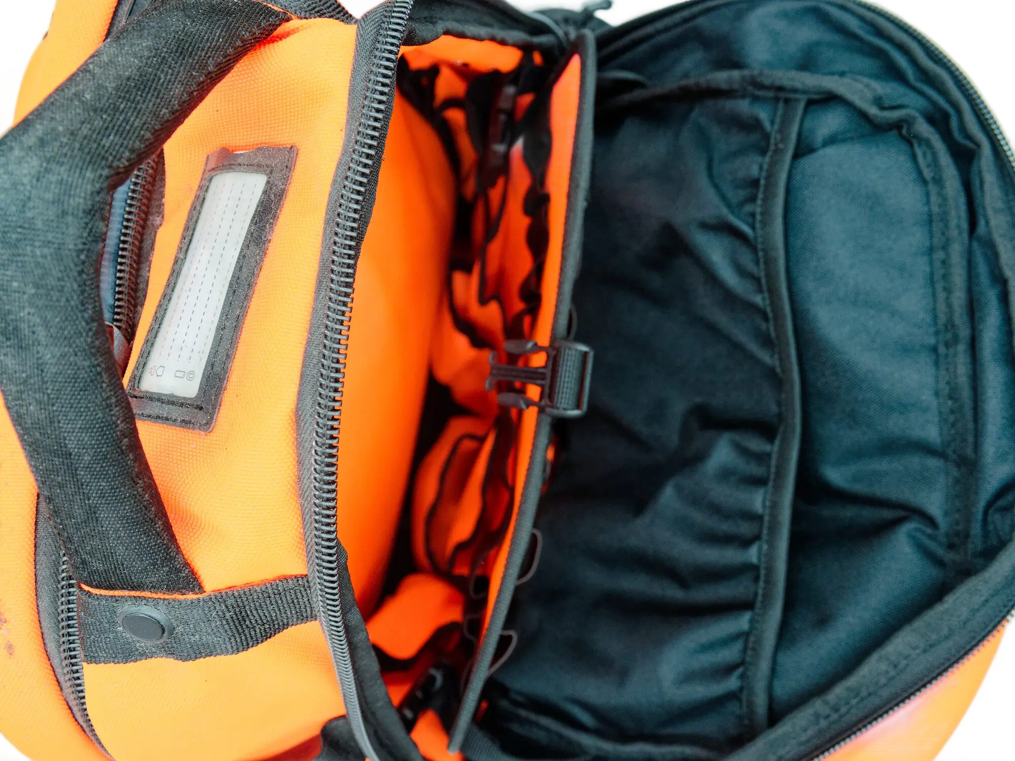 Top-down view into the open backpack showing the orange-lined interior, lid label, and heavy-duty zipper track