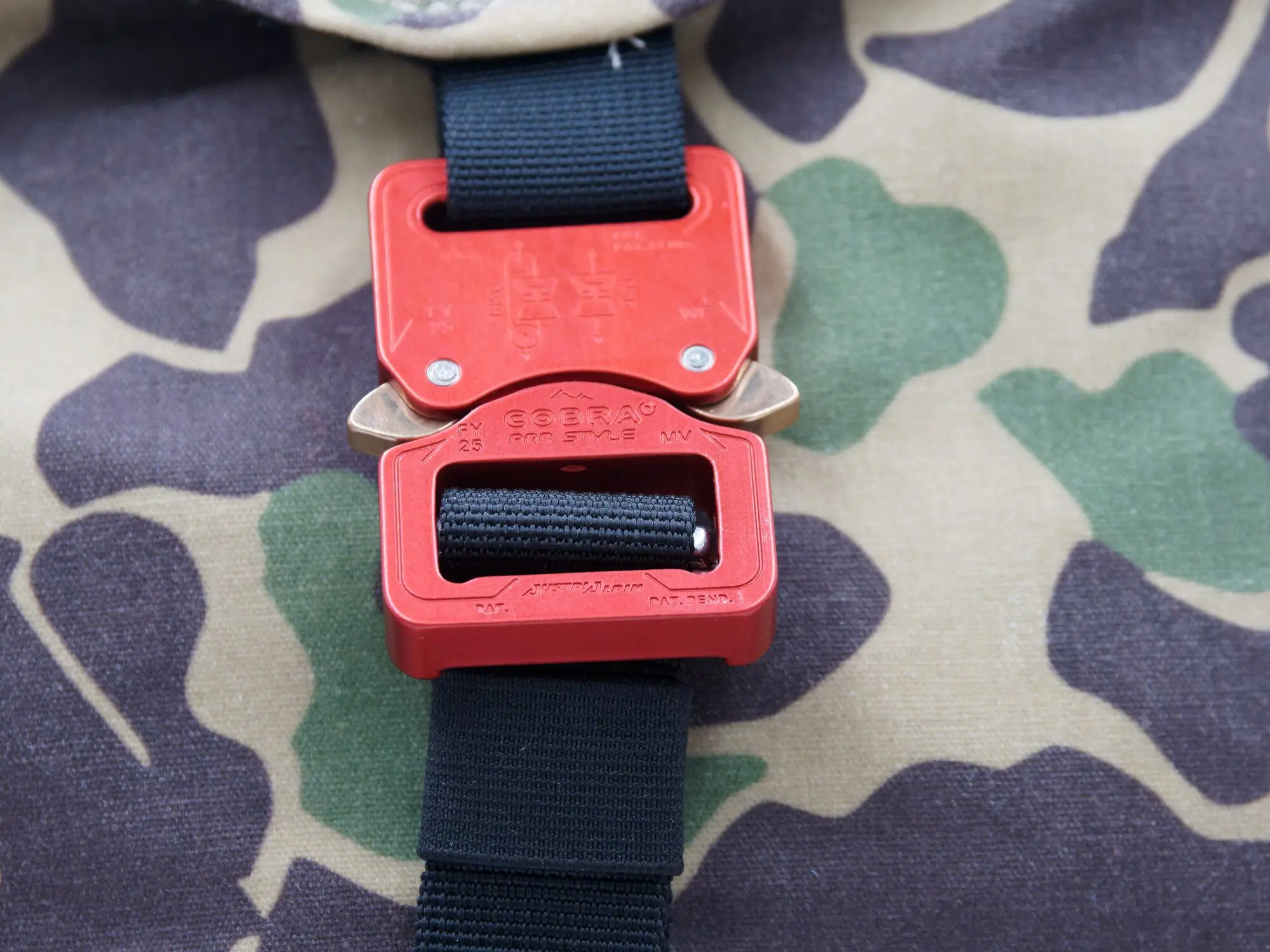 Close-up of the red patented AustriAlpin buckle with black webbing strap on camo canvas fabric