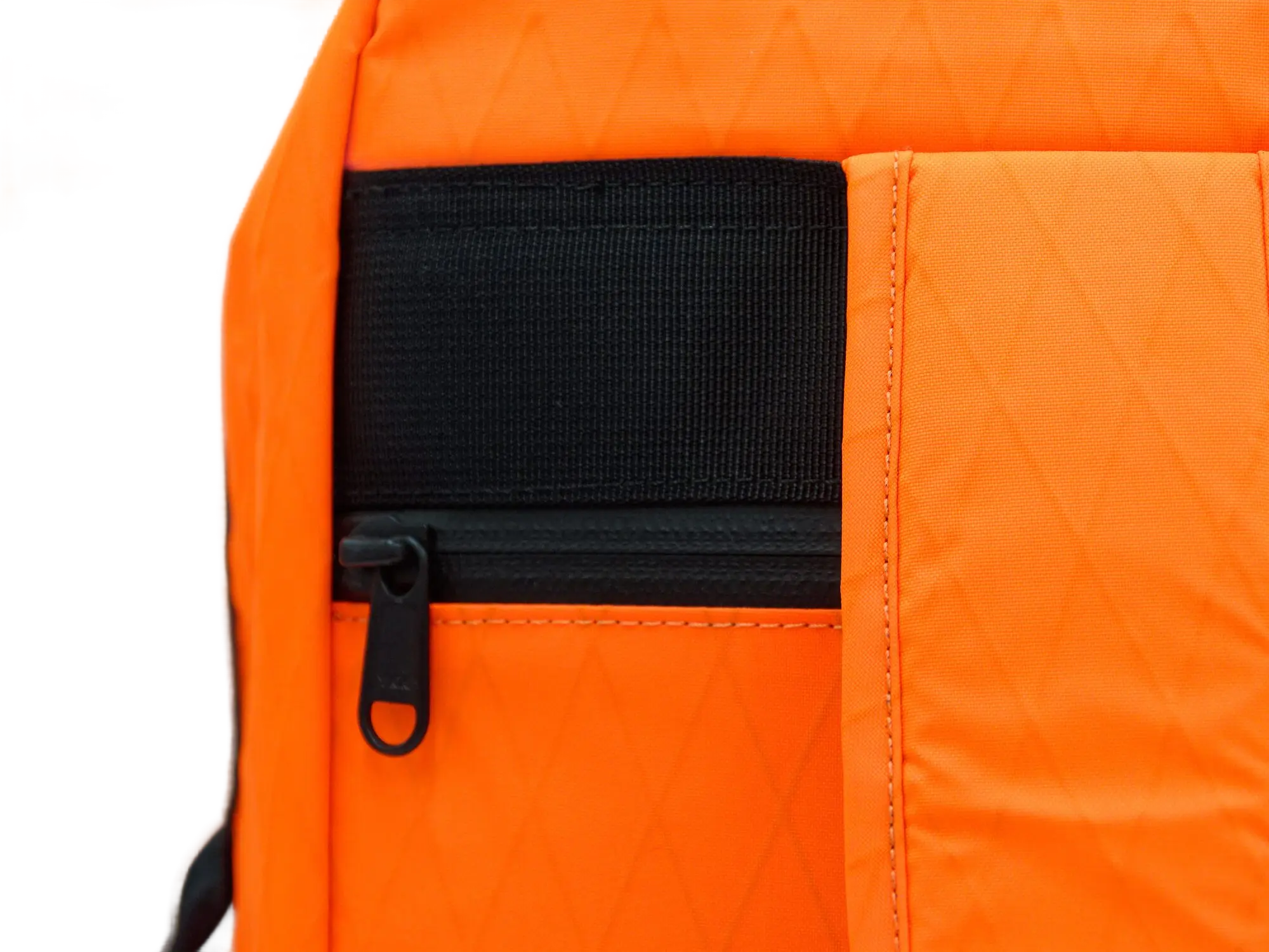 Close-up of the external side zippered pocket with black webbing on the orange X-Pac fabric