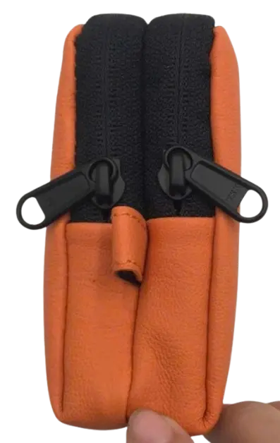 Top-down view of the orange leather pouch held in hand, showing two black zip pullers side by side