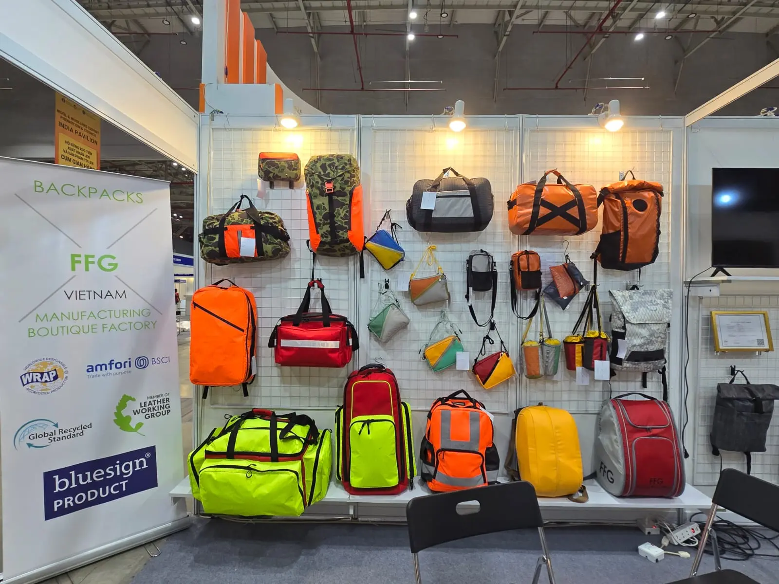Complete booth lineup: neon yellow, orange, black, red tactical backpacks and cargo bags on white gridded walls