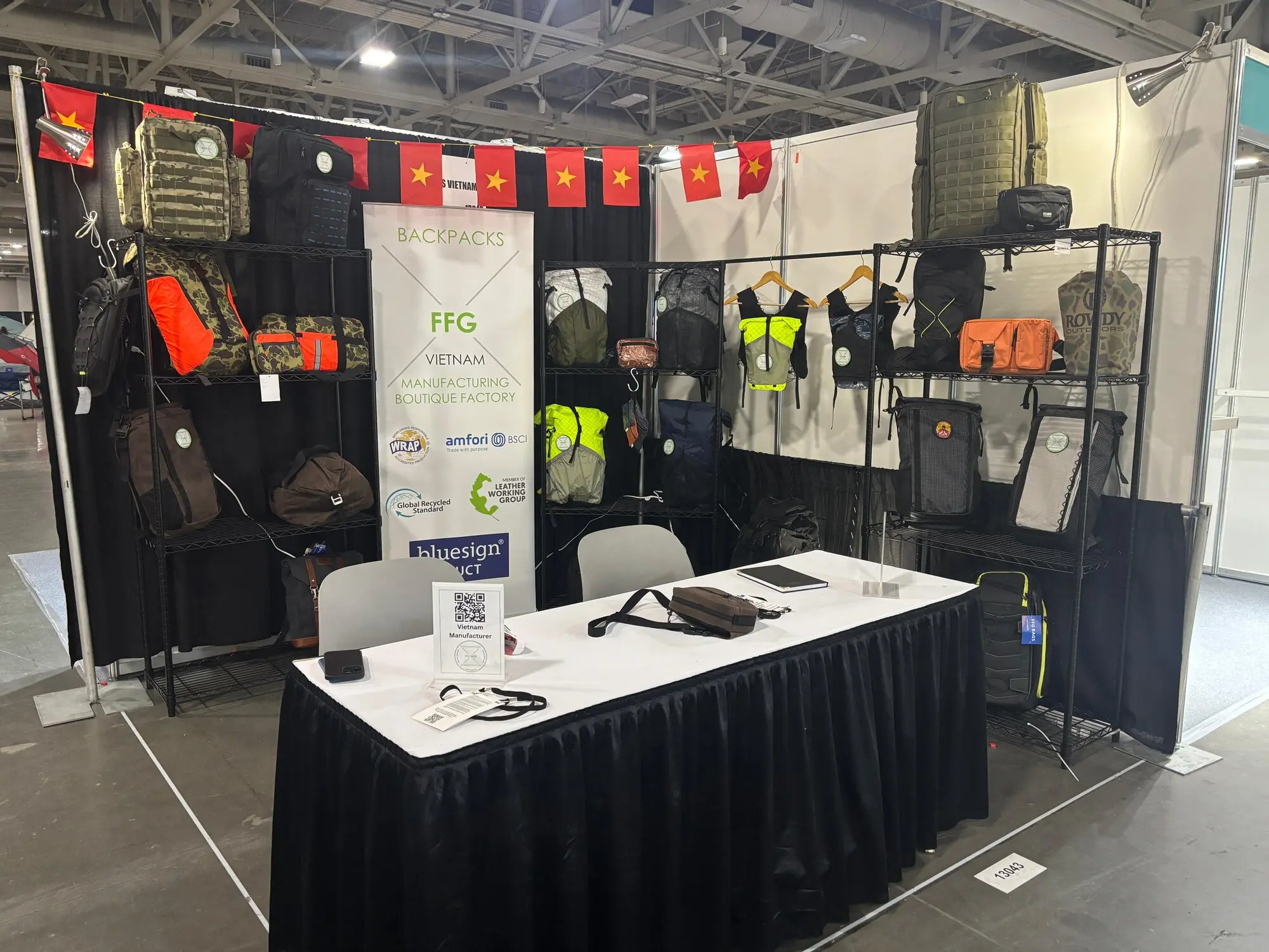 FFG Bags exhibition booth at Outdoor Retailer show with black-walled display featuring orange and green tactical backpacks, gear samples, branded signage, and information desk