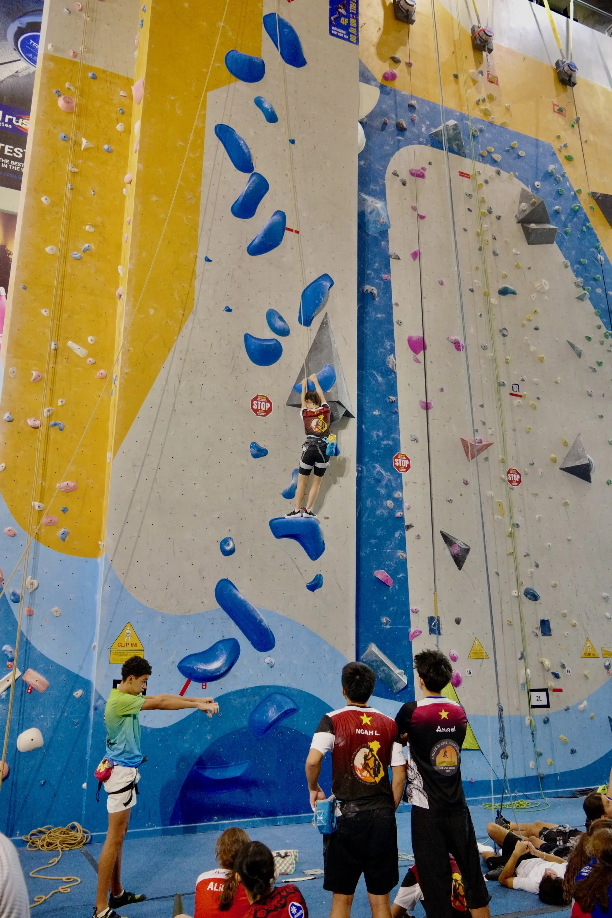 Female climber navigating turquoise and grey handholds on indoor competition wall
