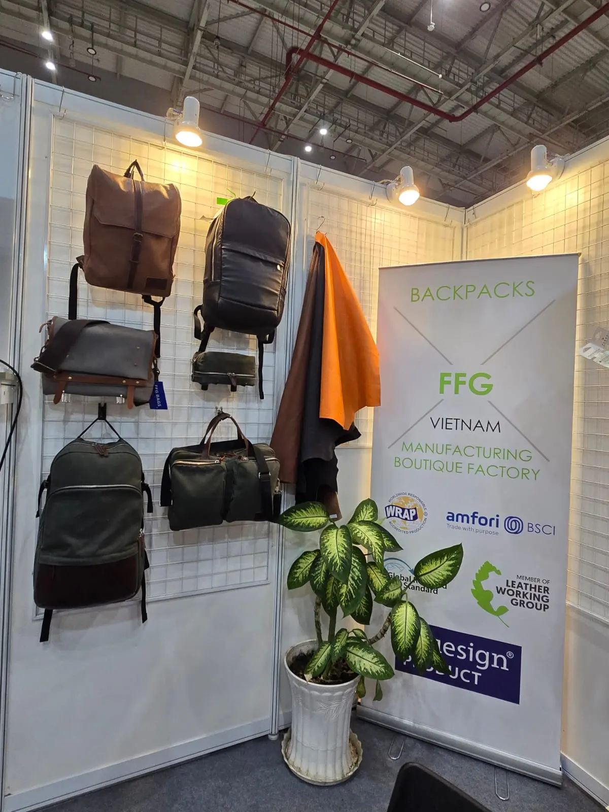 FFG booth panel with brown leather backpack, black and orange tactical packs, green potted plant, signage visible