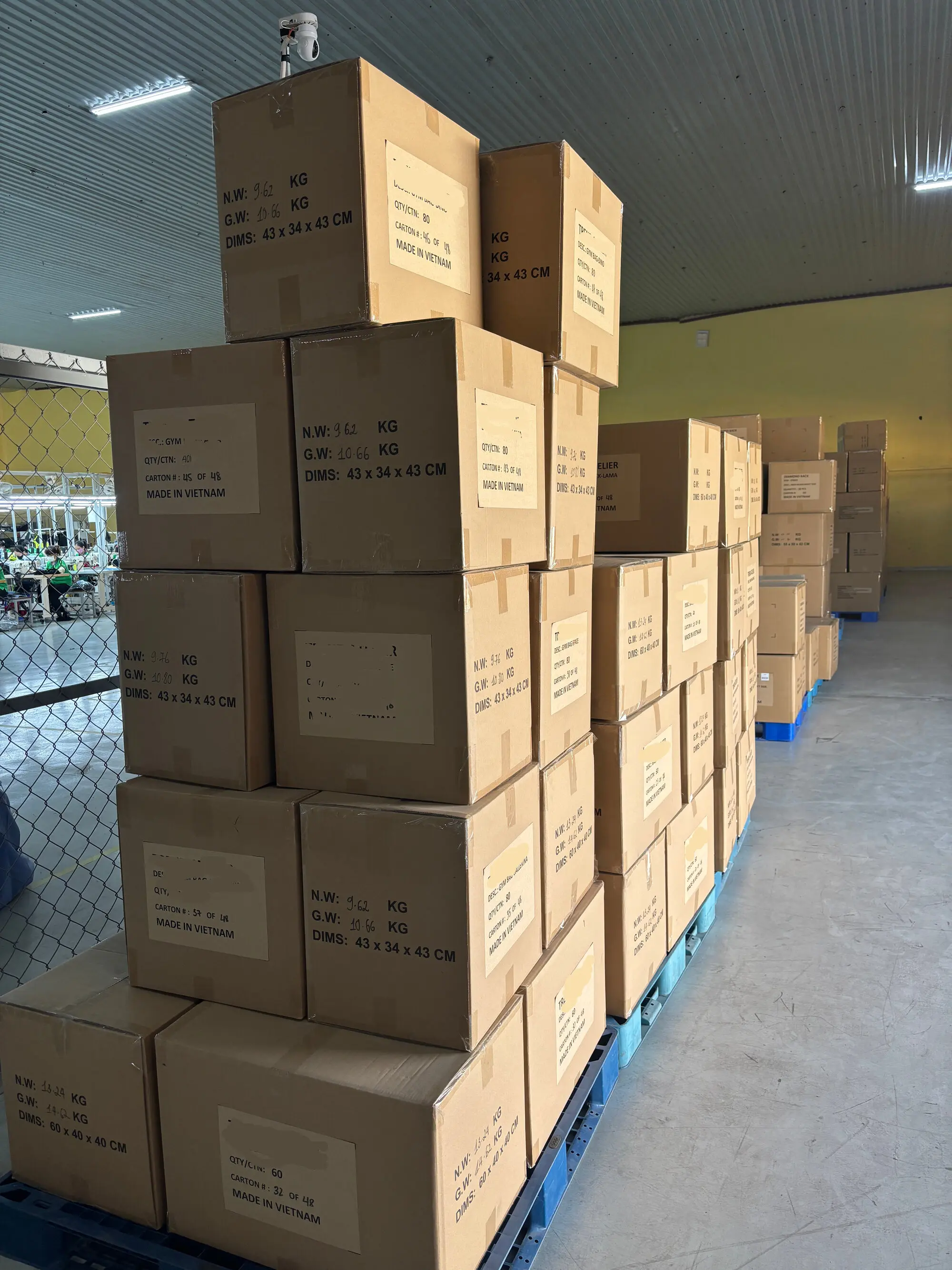 Stacked cardboard product boxes with printed labels and weight markings arranged on a blue pallet inside FFG warehouse