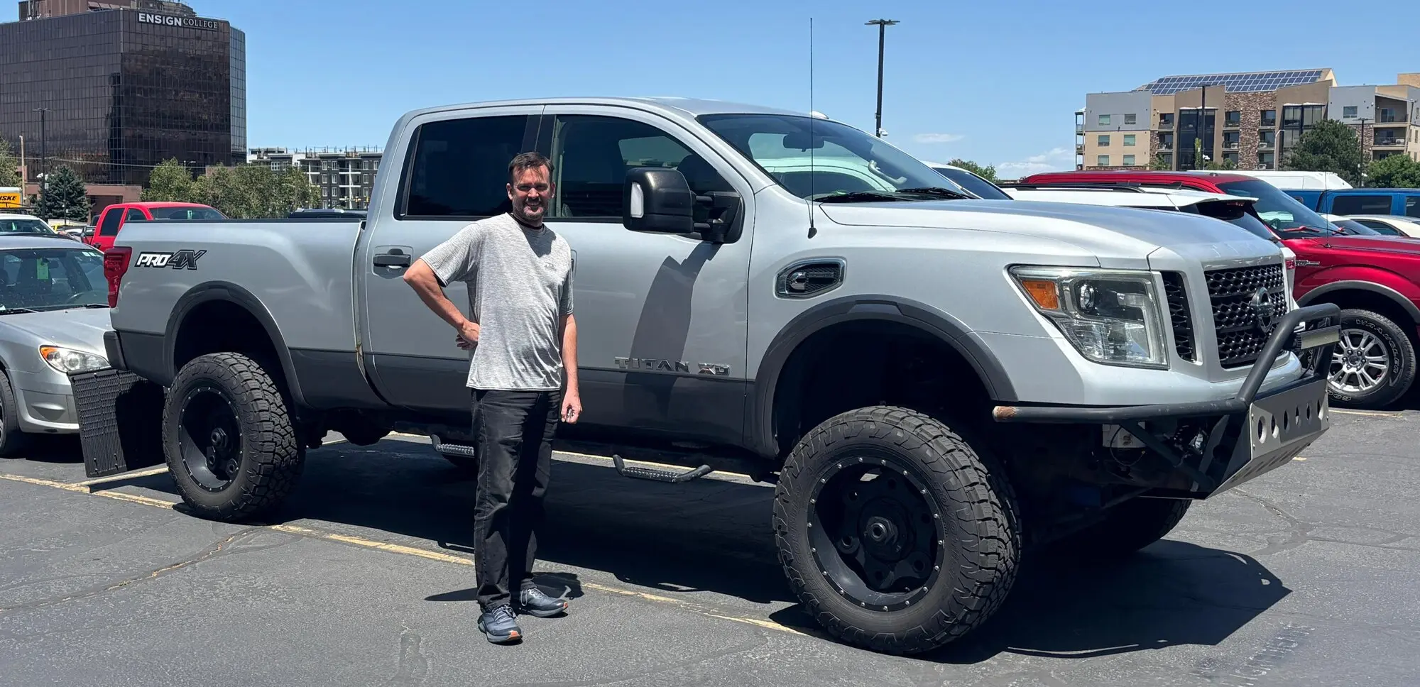 Man standing beside white Nissan Titan pickup truck in parking lot, illustrating tariff impact on US vehicle purchases